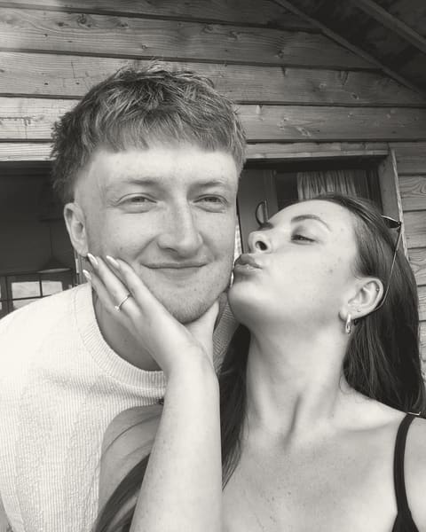 A kiss on the cheek outside a wooden cabin