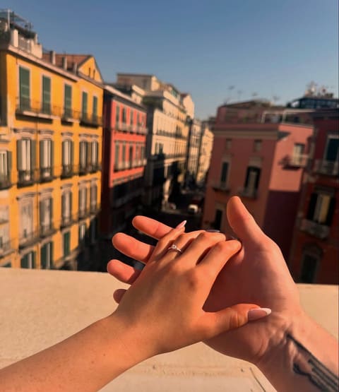 Their hands together on a sunny balcony, the engagement ring on her finger