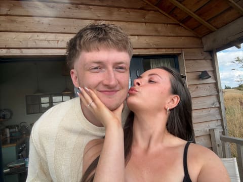 A kiss on the cheek outside a wooden cabin